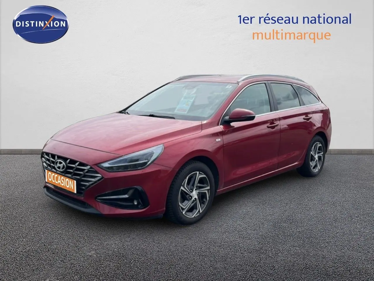 Vue 3/4 avant droite d'une Hyundai i30 SW 2023 rouge Sunset Red Metal avec jantes alliage et calandre distinctive.