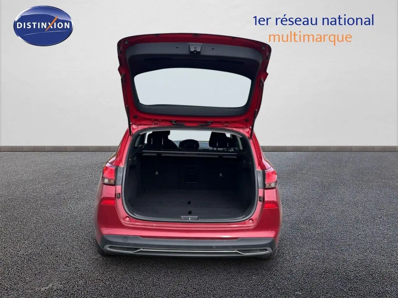 Vue arrière d'une Hyundai i30 SW 2023 rouge Sunset Red Metal avec coffre ouvert sur sol bitumé.