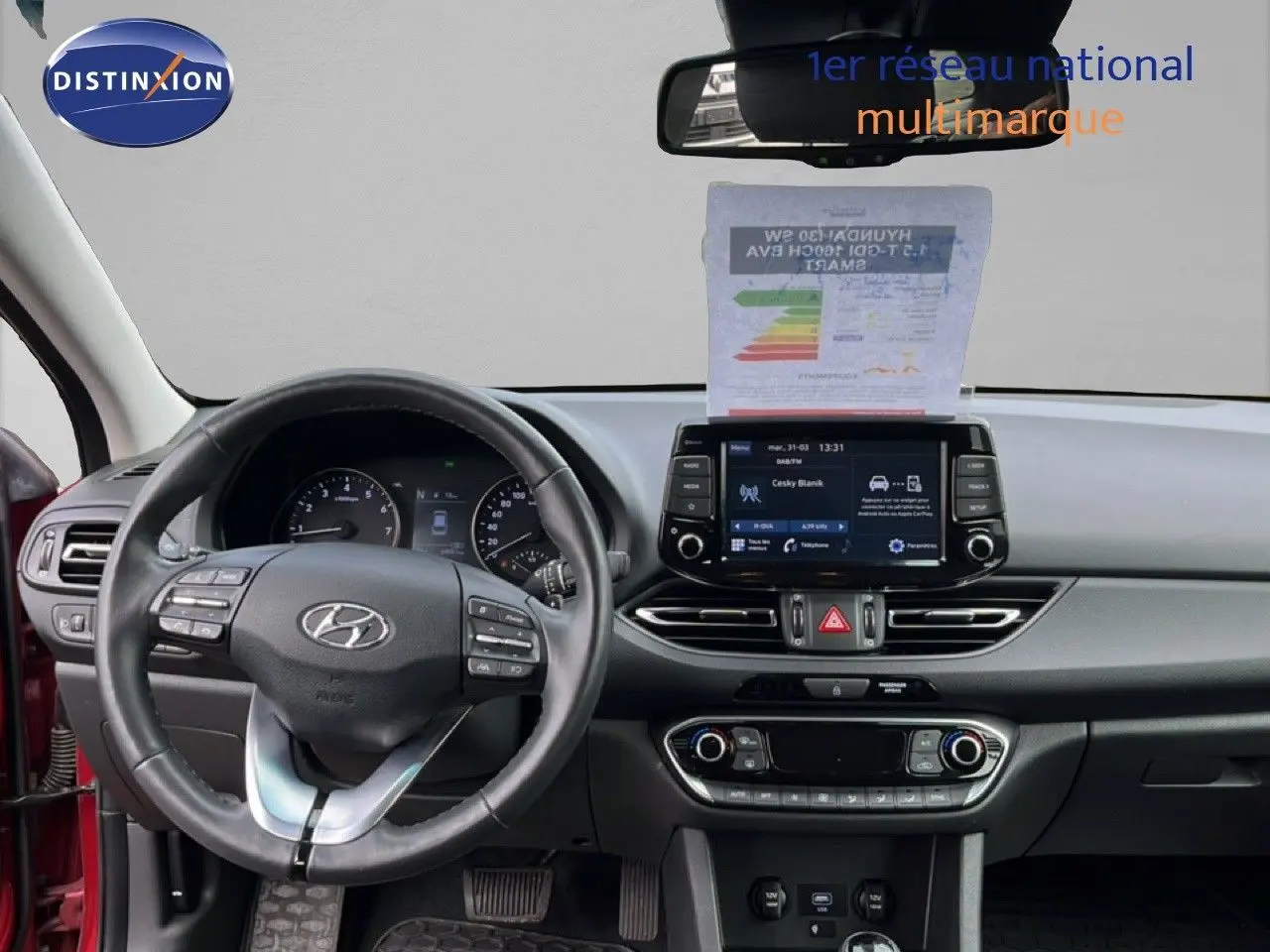 Vue intérieure frontale du tableau de bord de la Hyundai i30 SW 2023 en rouge Sunset avec écran tactile et volant cuir multifonction.