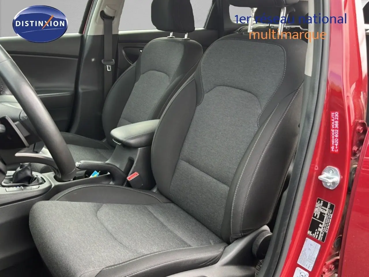 Vue intérieure côté conducteur du Hyundai i30 SW 2023, sièges tissu gris et cuir noir, portière rouge Sunset Red Metal ouverte.