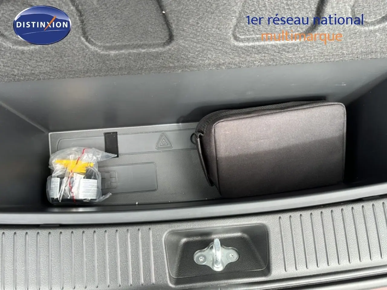 Coffre ouvert vu de dessus montrant un rangement avec une trousse noire et un kit emballé dans une Hyundai i30 SW rouge.