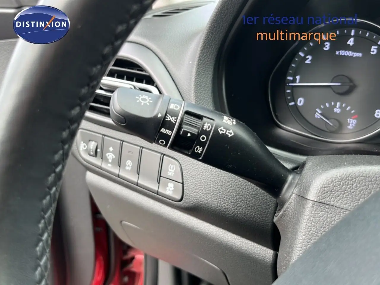 Gros plan sur la commande des feux et les boutons de réglage à gauche du volant dans l’habitacle d’une Hyundai i30 SW rouge.