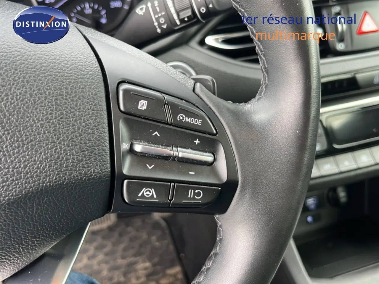 Gros plan sur le volant côté gauche du Hyundai i30 SW 2023 avec commandes multifonctions en plastique noir.