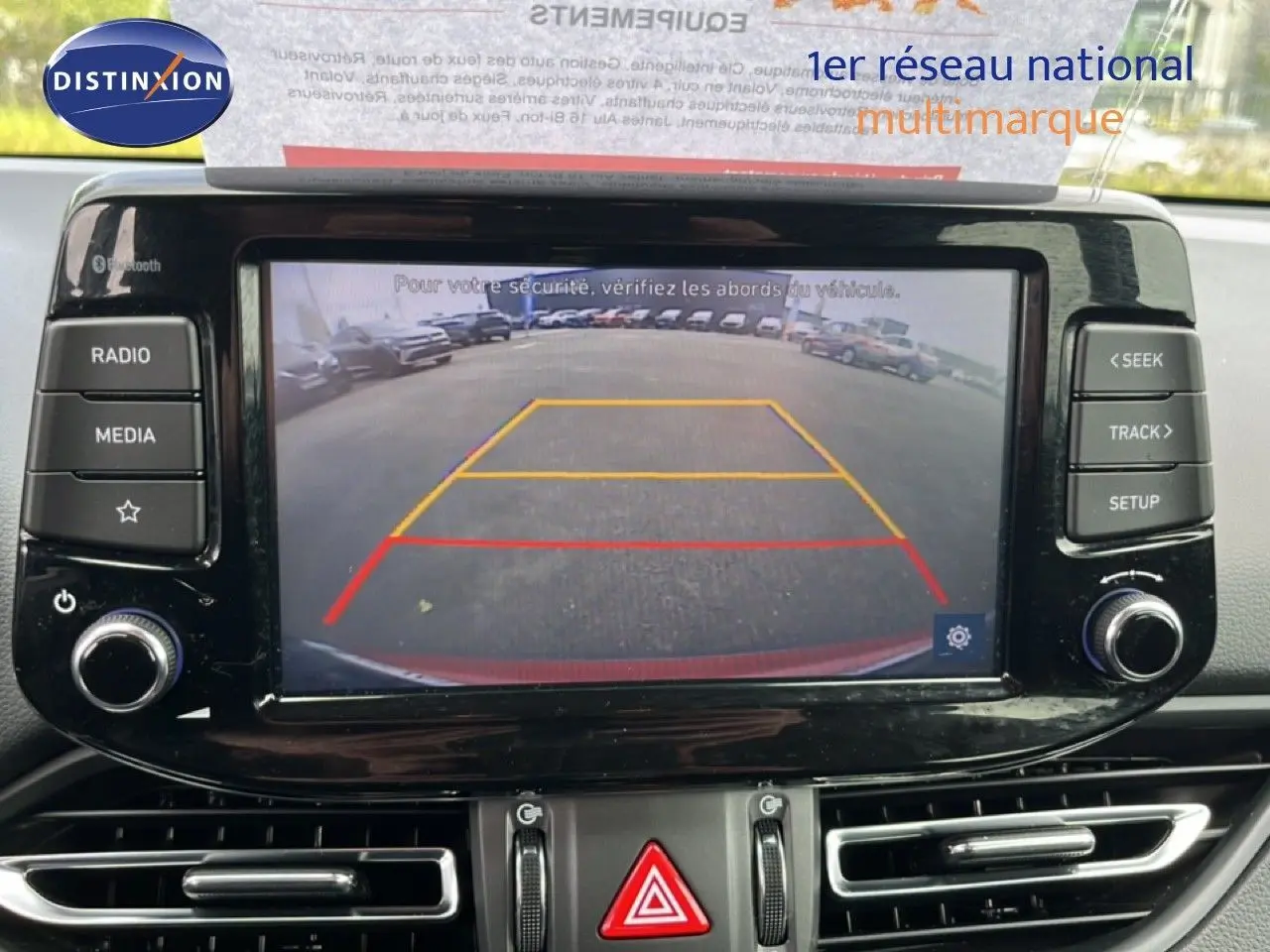 Vue intérieure de l’écran multimédia affichant la caméra de recul d’une Hyundai i30 SW rouge, avec commandes autour de l’écran.