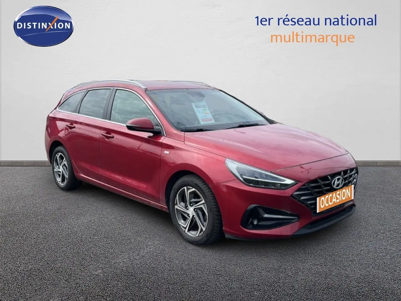 Vue 3/4 avant gauche d'une Hyundai i30 SW 2023 rouge Sunset Red Metal avec jantes bi-ton et calandre noire.