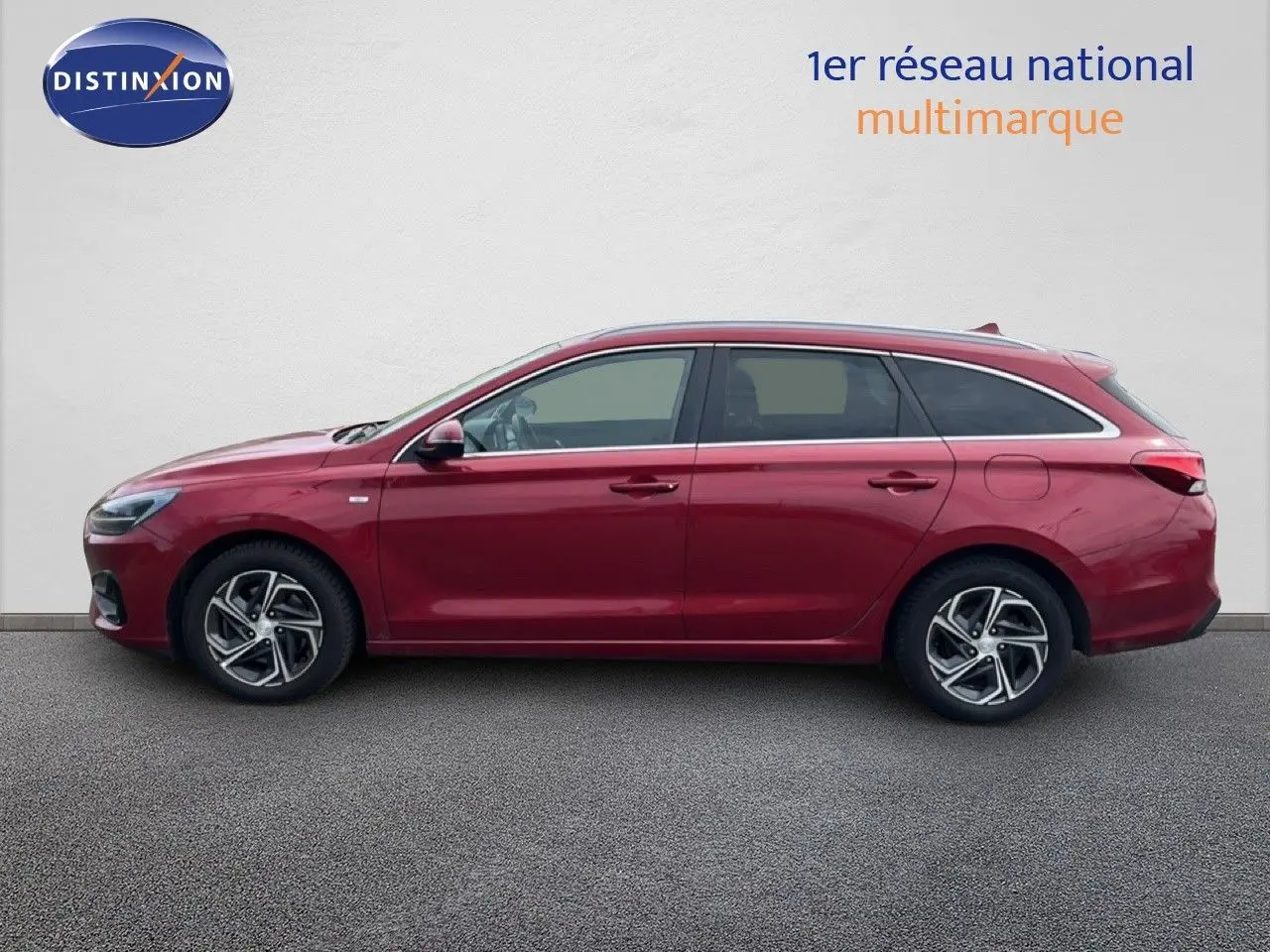 Vue de profil côté gauche d'une Hyundai i30 SW 2023 rouge Sunset Red Metal avec jantes alliage bi-ton.