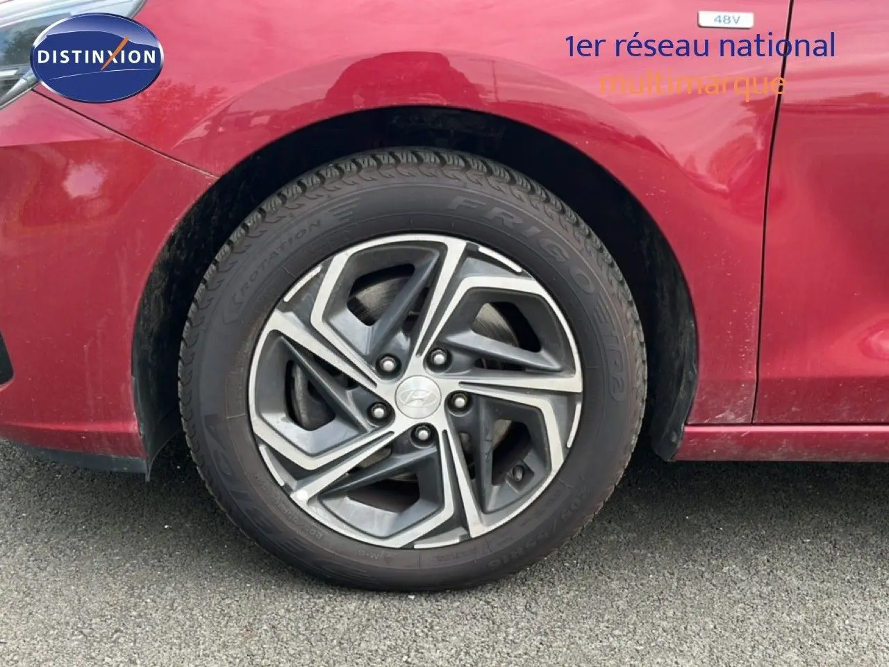Gros plan sur la roue avant gauche d'une Hyundai i30 SW 2023 en rouge Sunset Metal avec jante alliage bicolore.