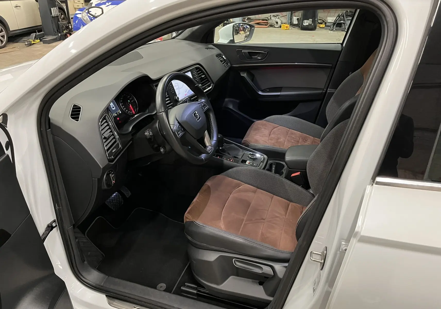 Vue intérieure côté conducteur du SEAT Ateca blanc, mettant en valeur les sièges bicolores marron et noir et le tableau de bord moderne.