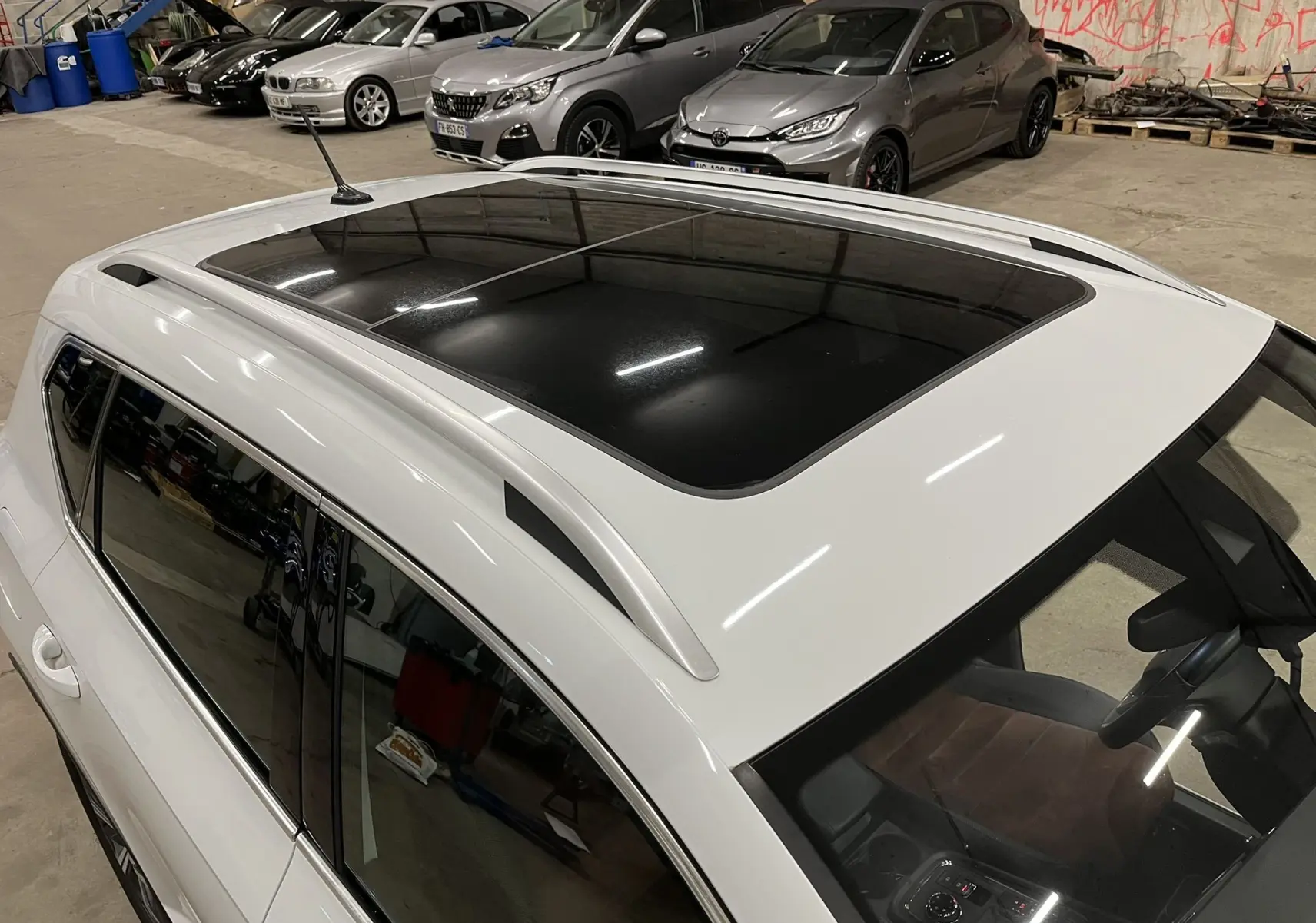 Vue plongeante sur le toit panoramique et la partie gauche d’un SEAT Ateca blanc stationné en intérieur.