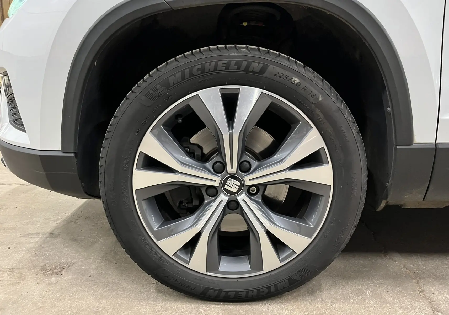 Gros plan sur la roue avant droite d’un SEAT Ateca blanc, mettant en valeur la jante alliage à design moderne.