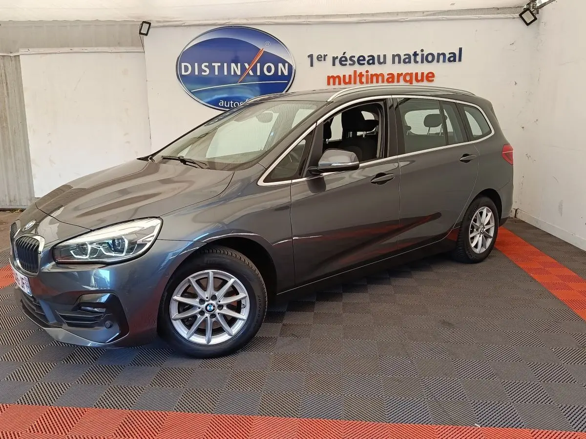 BMW Série 2 Gran Tourer gris clair vue 3/4 avant droit, avec jantes alliage et feux LED allumés.