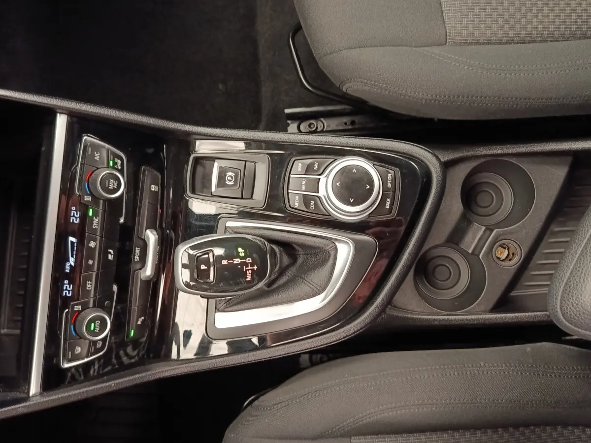 Vue plongeante sur la console centrale noire brillante de la BMW Série 2 Gran Tourer avec levier de vitesse automatique et commandes climatisation.