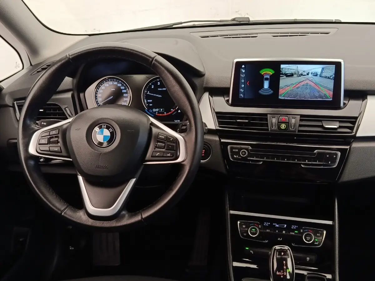 Vue intérieure centrée sur le volant cuir et alu de la BMW Série 2 Gran Tourer 218i avec écran multimédia allumé.