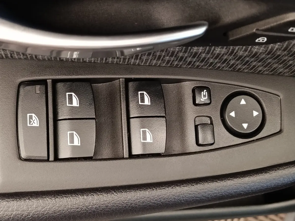 Gros plan sur les commandes de lève-vitres et rétroviseurs noirs dans la porte côté conducteur d'une BMW Série 2 Gran Tourer gris clair.