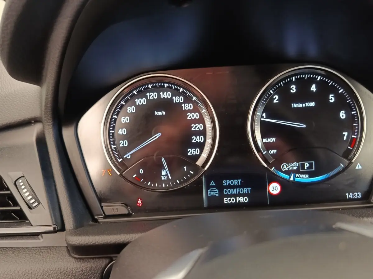 Gros plan sur le tableau de bord numérique de la BMW Série 2 Gran Tourer 218i, affichant modes de conduite et compte-tours.