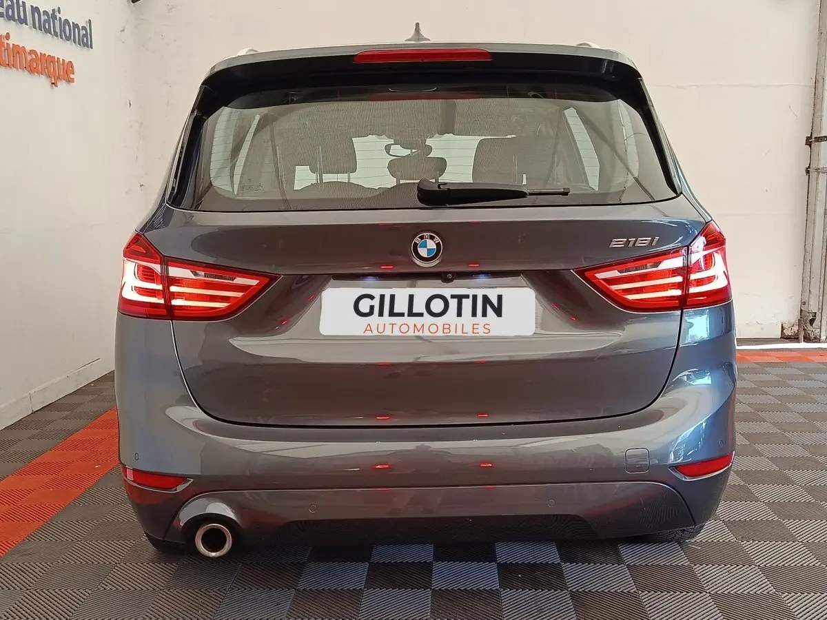 Vue arrière d'une BMW Série 2 Gran Tourer 218i Lounge gris clair avec feux LED allumés en intérieur showroom.