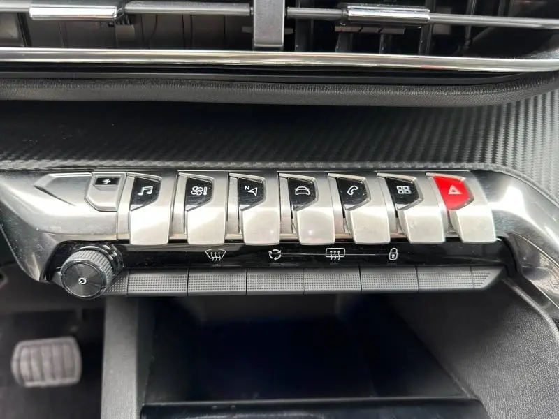 Gros plan sur la rangée de boutons métalliques du tableau de bord du Peugeot 3008 Hybride Rechargeable noir, avec symbole d'alerte rouge.