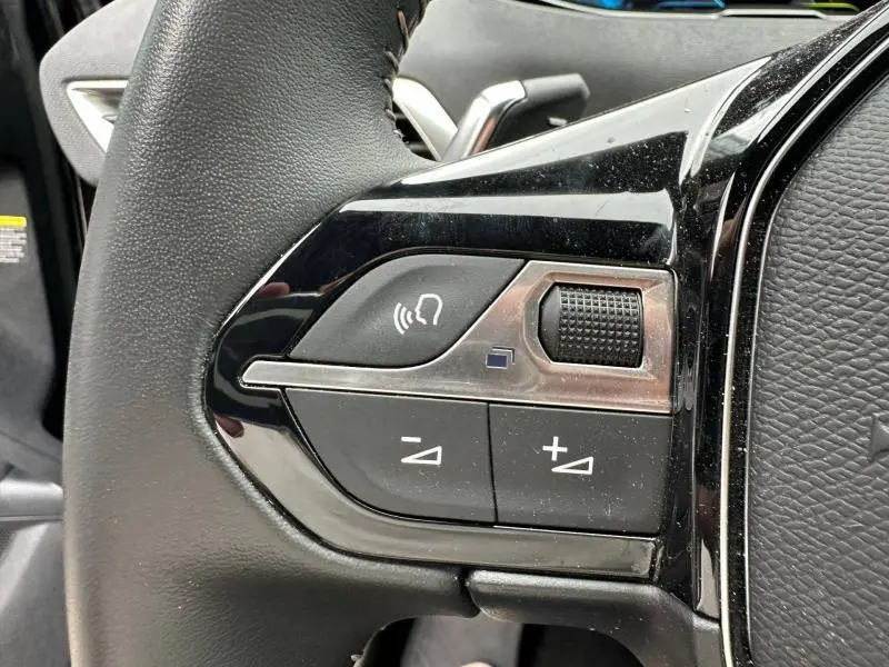 Gros plan sur les commandes gauche du volant cuir noir du Peugeot 3008 Hybride Rechargeable 2024, boutons de volume et appel mains-libres.