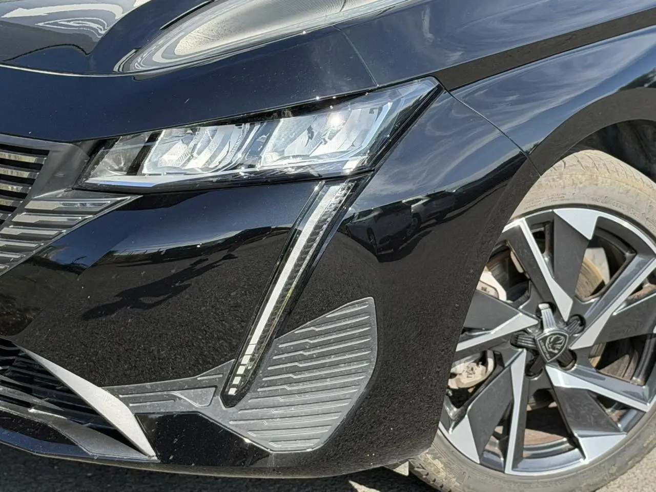 Gros plan sur l’avant droit noir Perla d’une Peugeot 308 SW 2025, mettant en valeur les phares LED et jantes alliage 17 pouces.