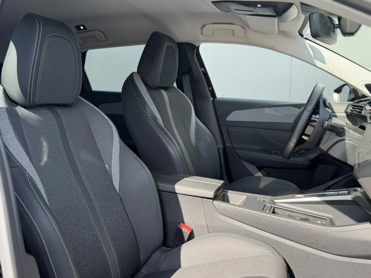 Vue intérieure côté droit de la Peugeot 308 SW 2025, sièges avant en sellerie tri matières noire avec surpiqûres bleues.