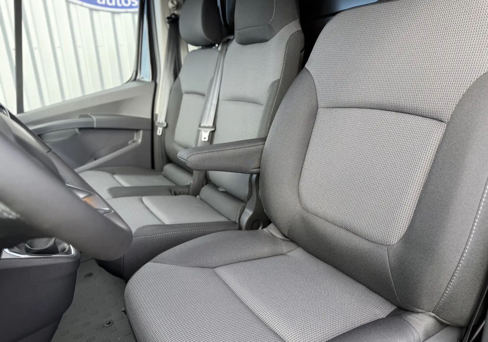 Gros plan sur les sièges avant gris tissu du Renault Trafic Fourgon noir crépuscule, vue depuis le côté gauche intérieur.