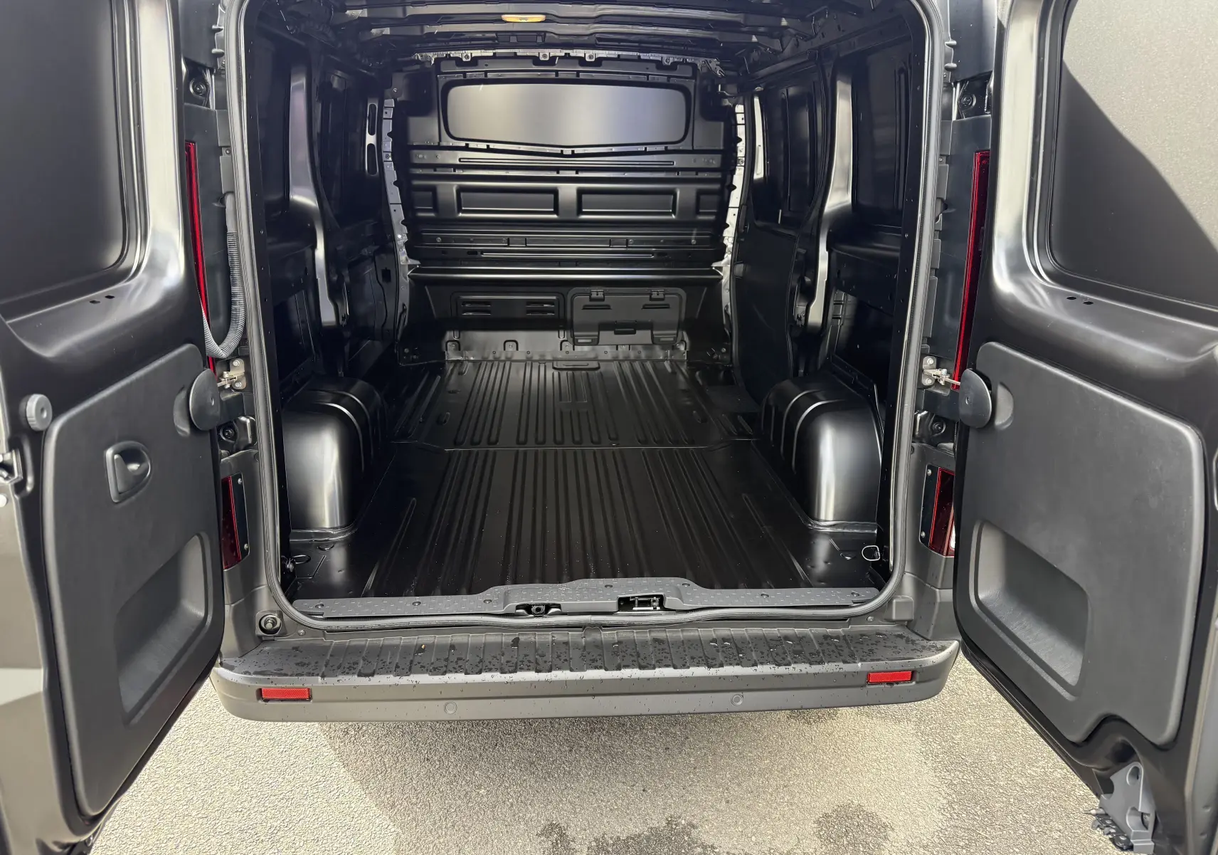 Vue arrière du Renault Trafic Fourgon noir crépuscule avec portes ouvertes montrant l’espace de chargement vide et spacieux.