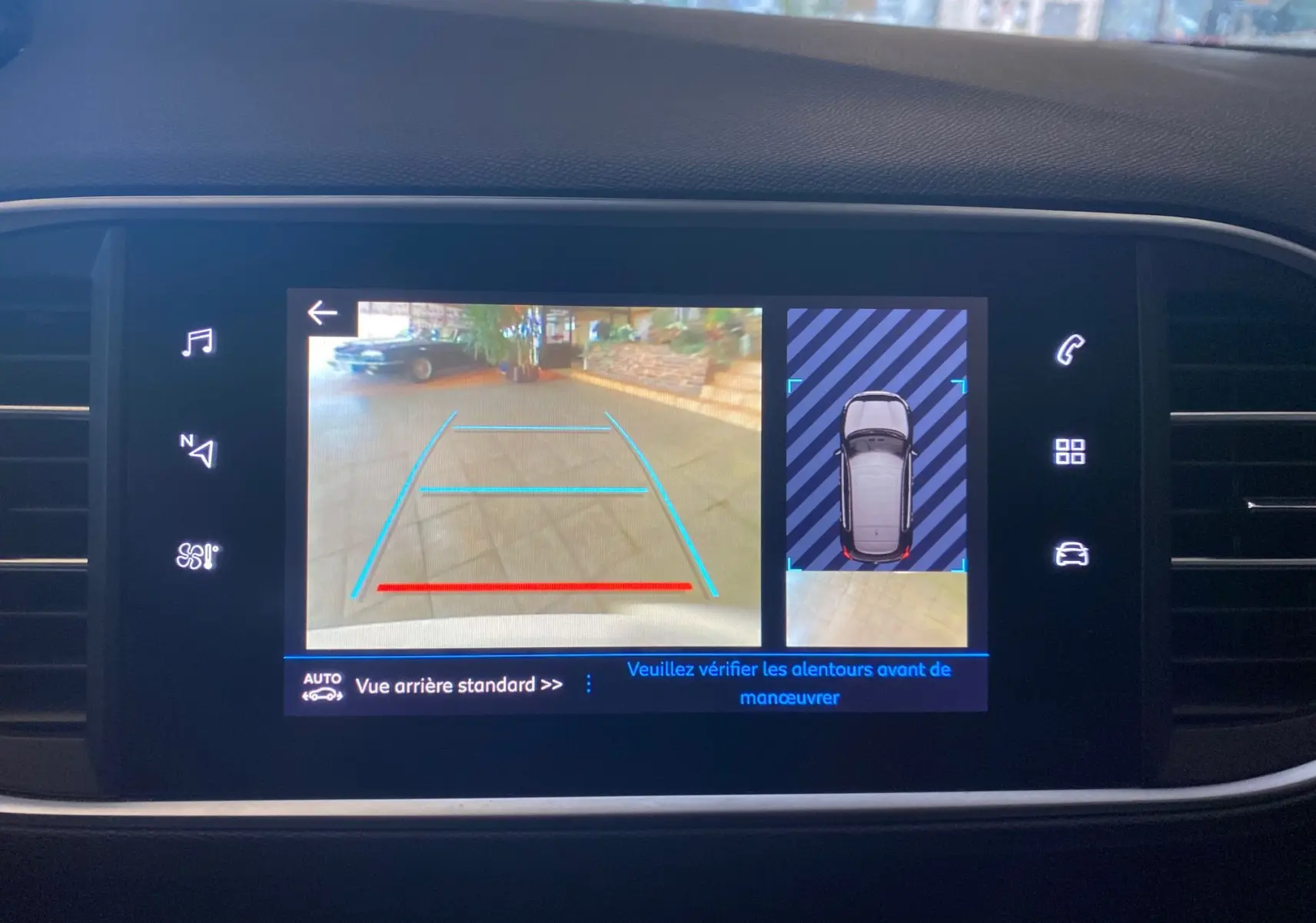 Écran tactile intérieur montrant la caméra de recul et l'aide au stationnement du Peugeot 308 blanc, version allure 2020.