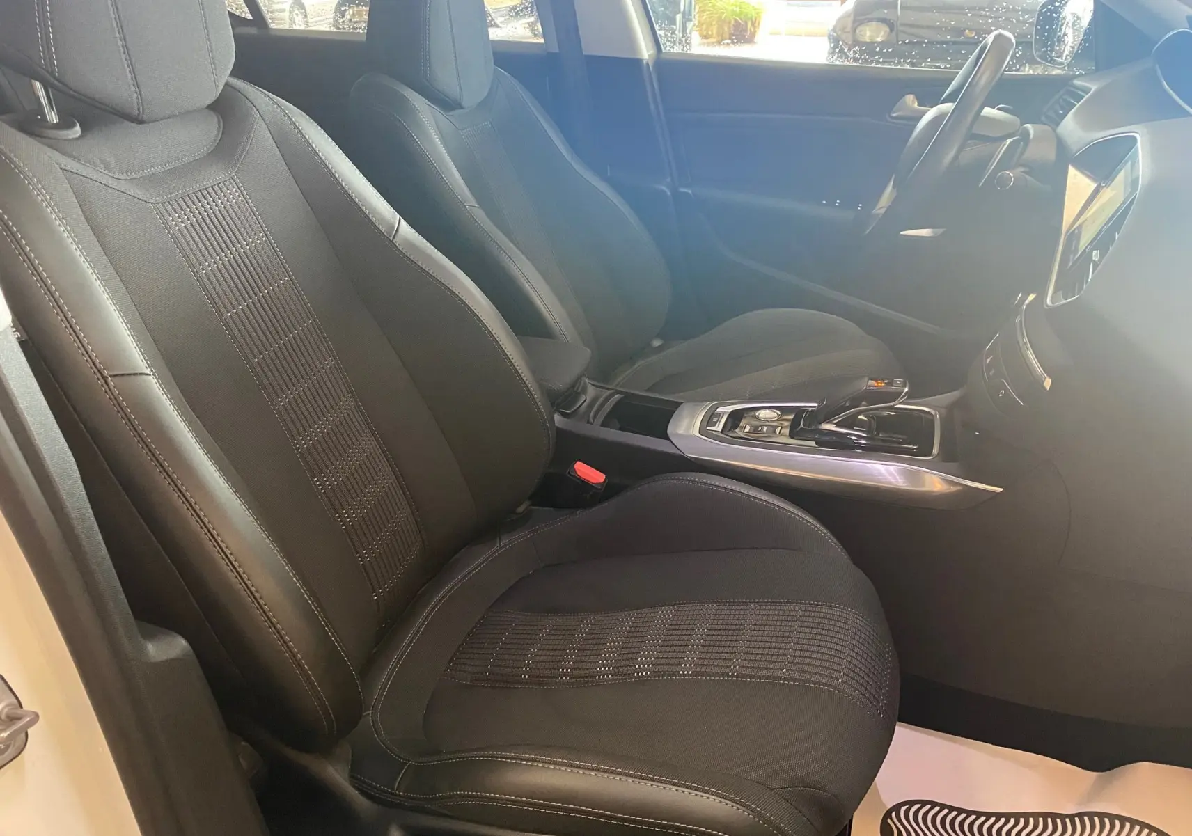 Vue intérieure côté conducteur de la Peugeot 308 Allure blanche de 2020, sièges tissu noir et console centrale moderne.