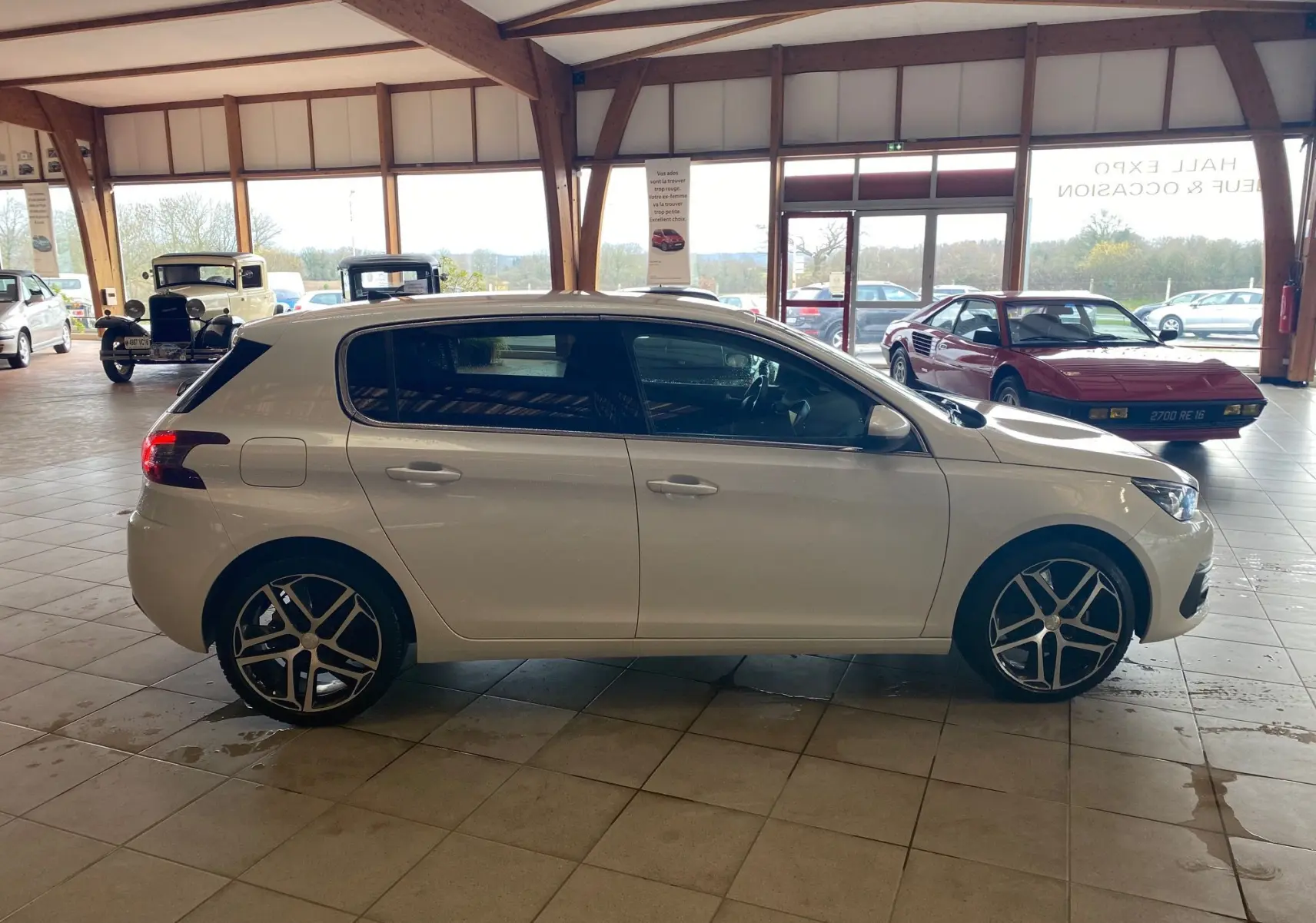 Profil côté droit d'une Peugeot 308 blanche 5 portes avec jantes alliage, dans un showroom lumineux.