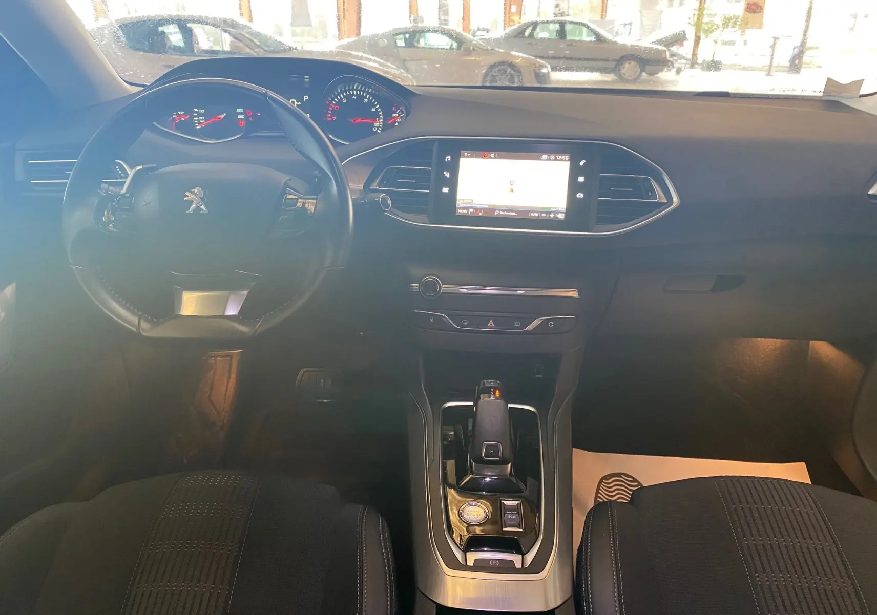 Vue intérieure frontale du tableau de bord et console centrale noire d'une Peugeot 308 blanche de 2020 avec écran tactile et volant compact.
