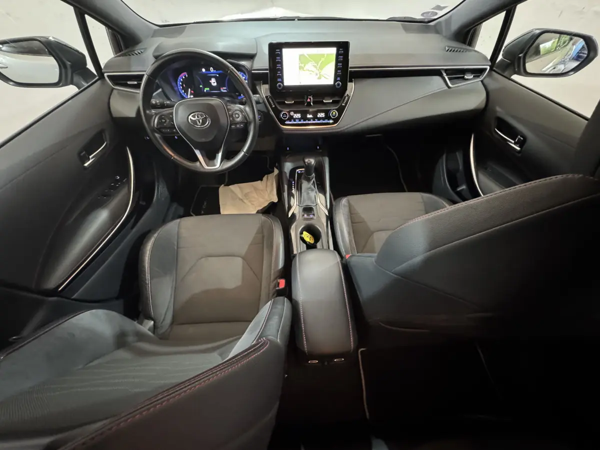 Intérieur noir de la Toyota Corolla Hybride 122h Collection 2021 vu de l'arrière, tableau de bord et écran tactile central visibles.