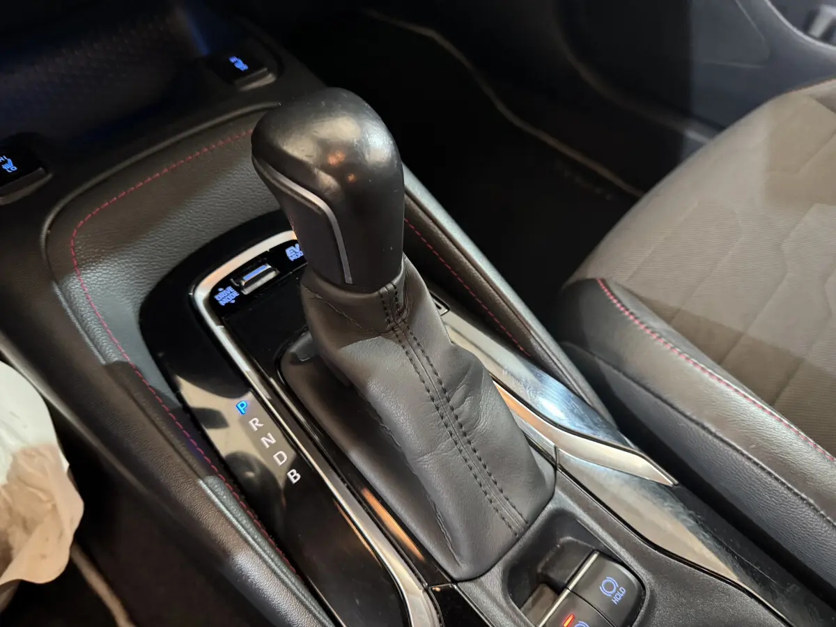 Le levier de vitesses automatique en cuir noir avec surpiqûres rouges dans une Toyota Corolla Hybride gris clair, vue intérieure rapprochée.
