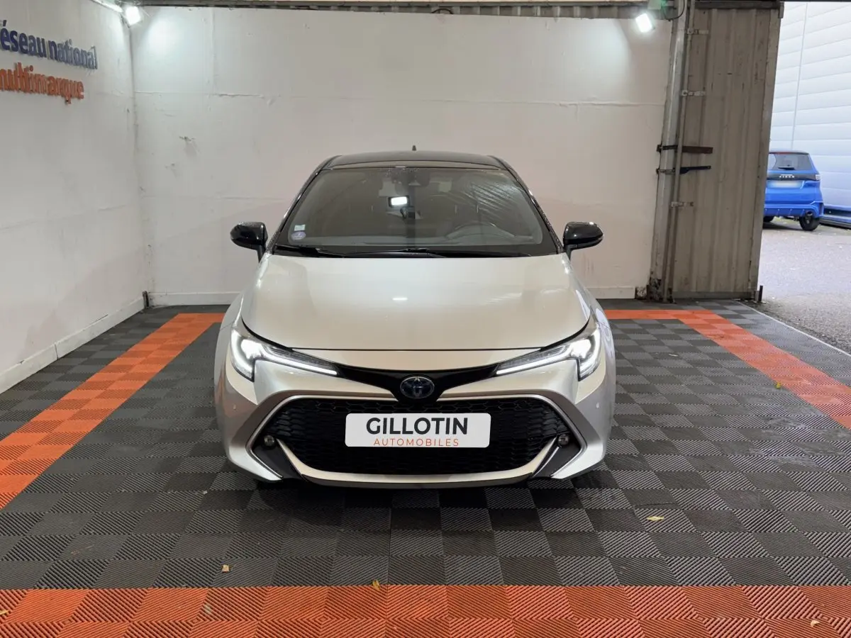 Toyota Corolla Hybride 122h Collection gris clair vue de face dans un garage avec sol à damiers noir et orange