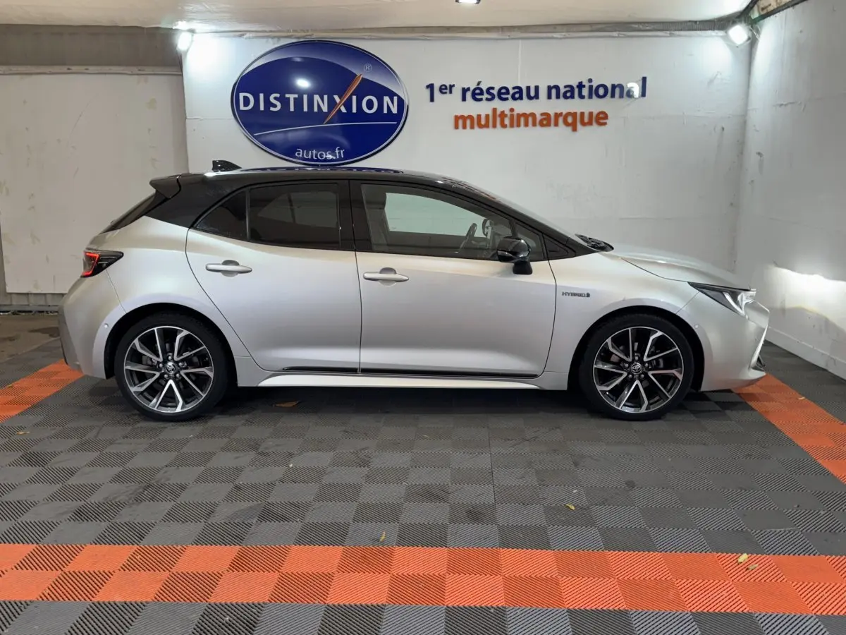 Profil côté gauche d'une Toyota Corolla Hybride 122h Collection gris clair avec toit noir en intérieur showroom.