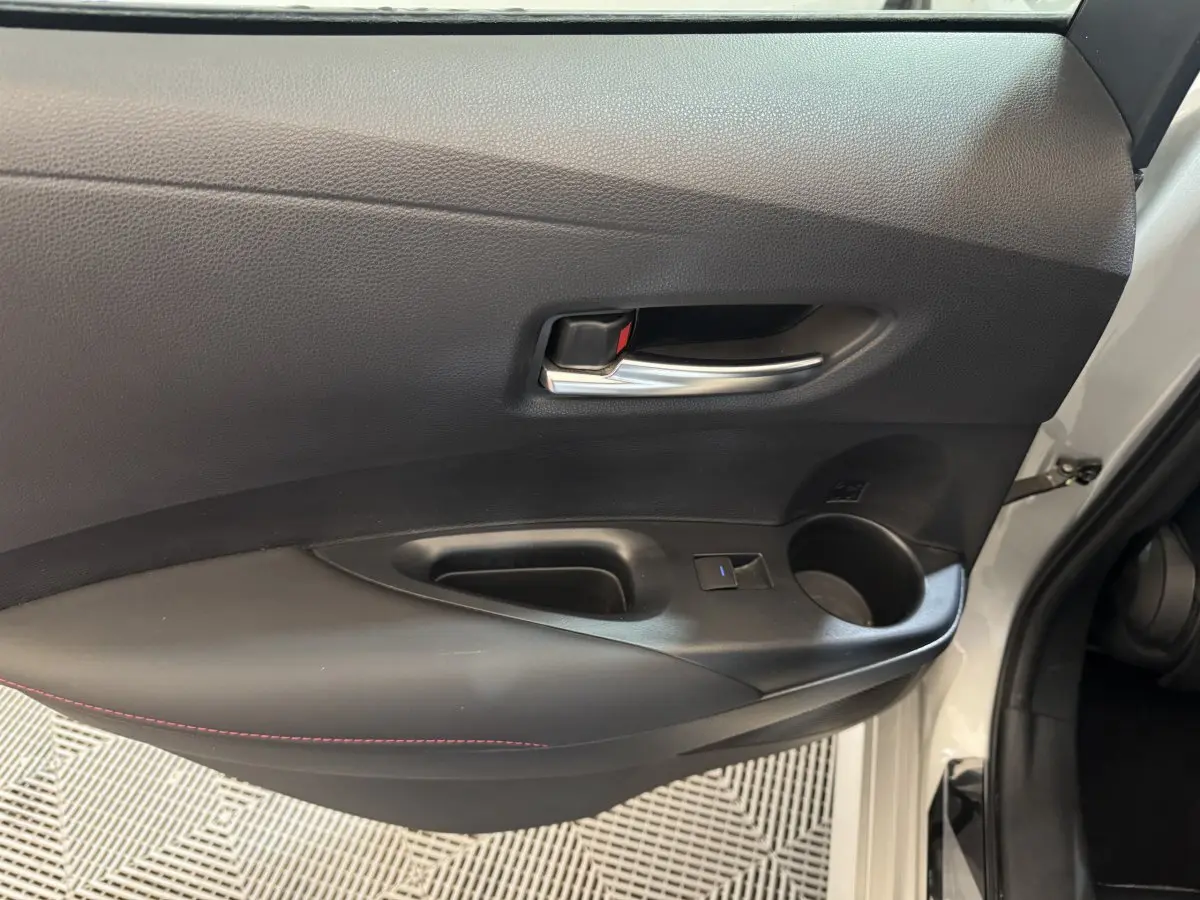Vue rapprochée de la porte avant gauche gris clair de la Toyota Corolla Hybride 122h avec poignée intérieure chromée et accoudoir noir.