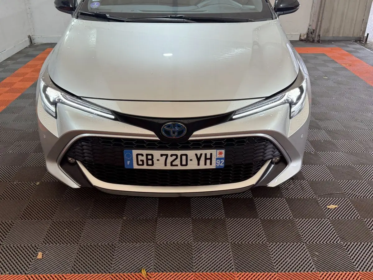 Vue frontale d'une Toyota Corolla Hybride 122h Collection gris clair avec calandre noire et phares LED fins.