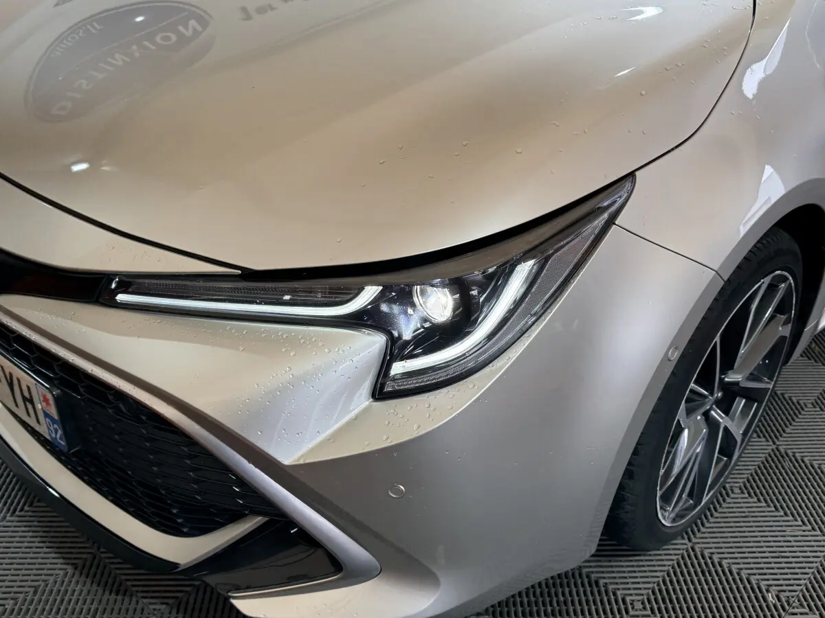 Gros plan sur l'avant droit gris clair d'une Toyota Corolla hybride 2021, mettant en valeur le phare LED et la jante alliage.