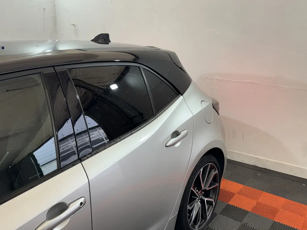 Vue côté arrière droit d'une Toyota Corolla hybride gris clair avec toit noir et jantes alliage sport.