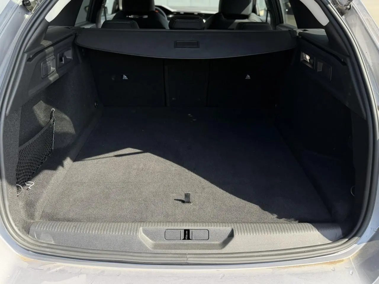 Coffre ouvert d’un Peugeot 308 SW gris Artense, montrant l’espace de chargement vide et la moquette noire.