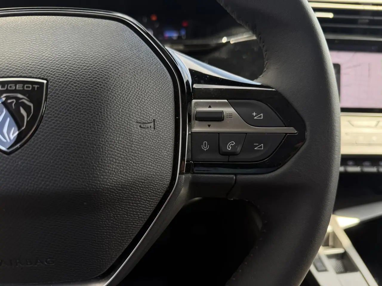Gros plan sur le volant cuir noir du Peugeot 308 SW 2025 avec commandes intégrées et écran tactile flou en arrière-plan.