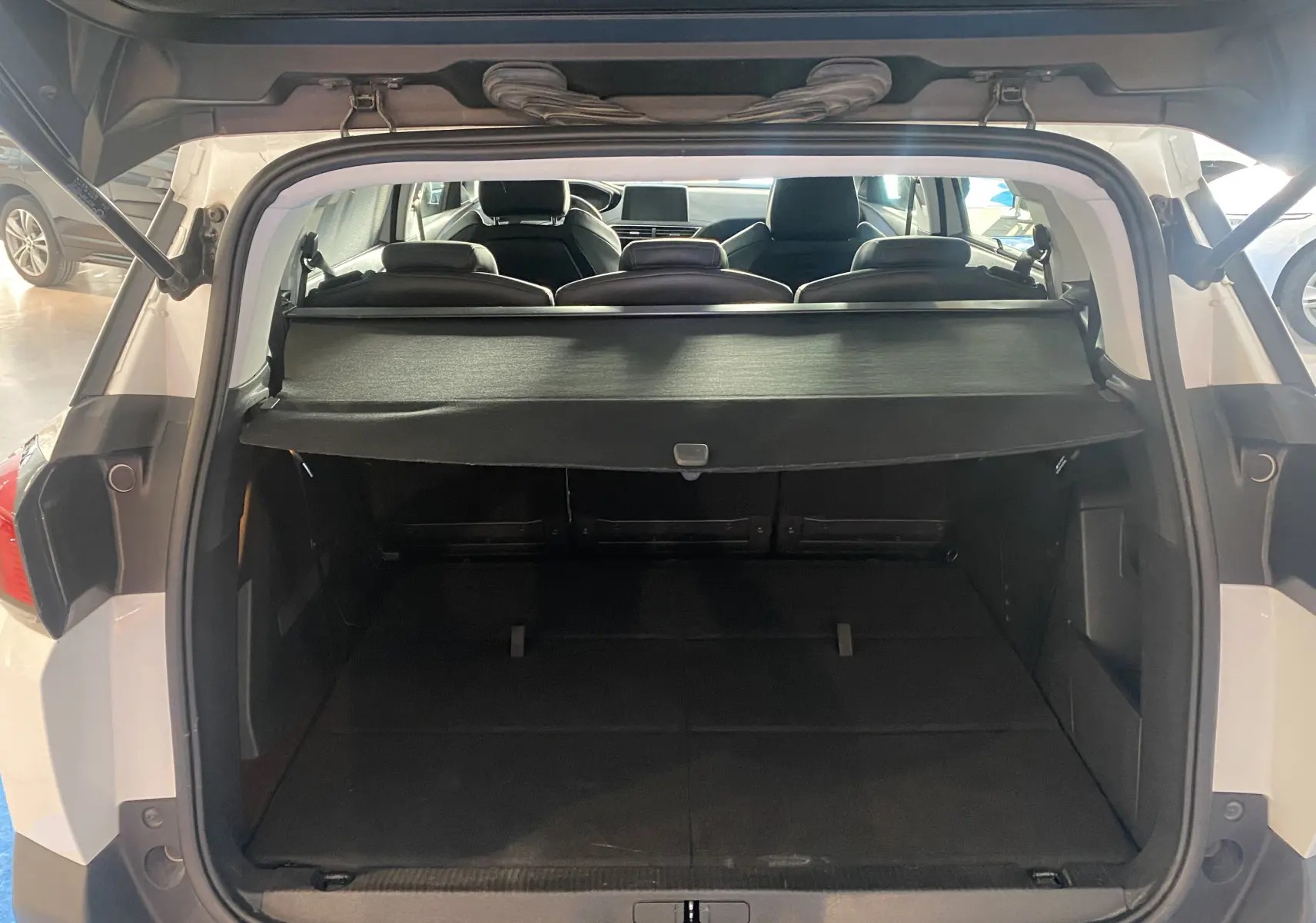 Coffre ouvert d'un Peugeot 5008 blanc blanquise, vue arrière montrant l'espace de chargement et la plage arrière noire.
