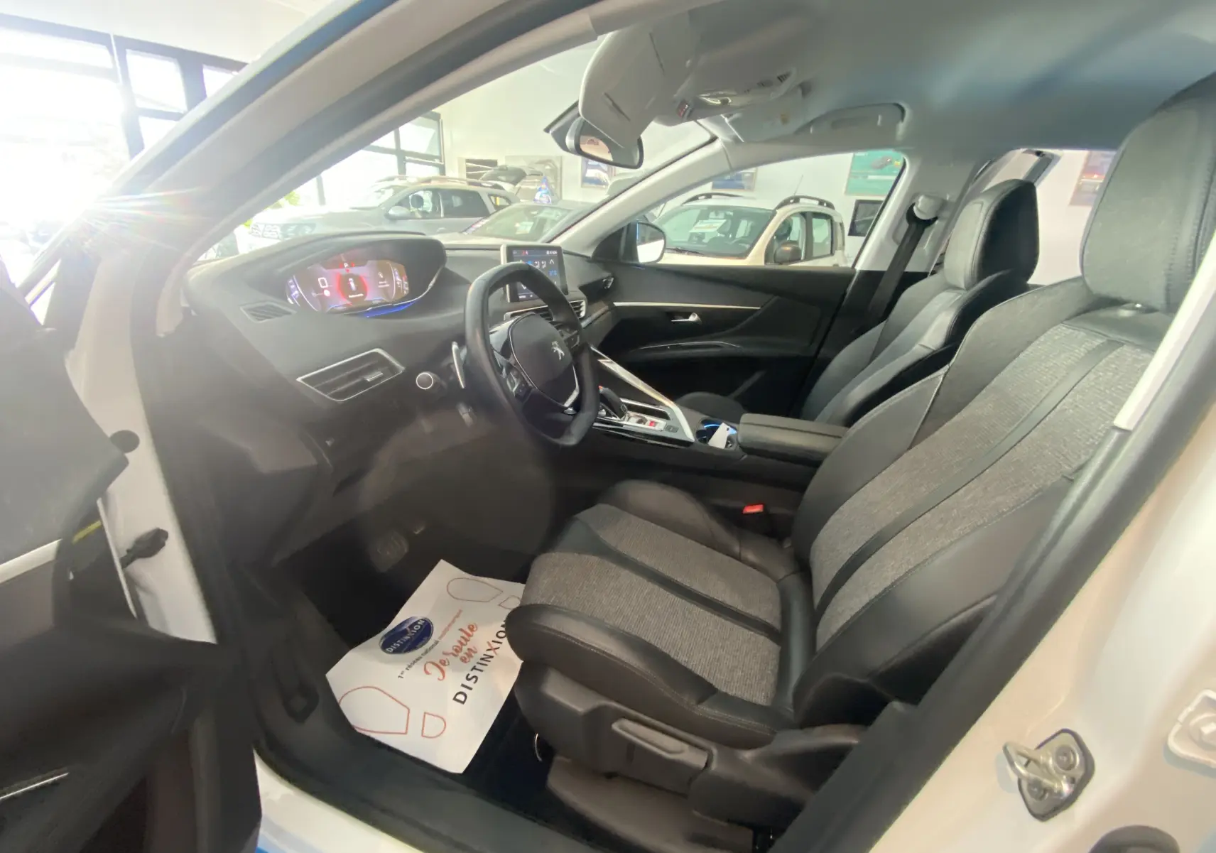 Vue intérieure côté conducteur du Peugeot 5008 blanc, mettant en valeur les sièges bi-matière gris et noir et le tableau de bord digital.