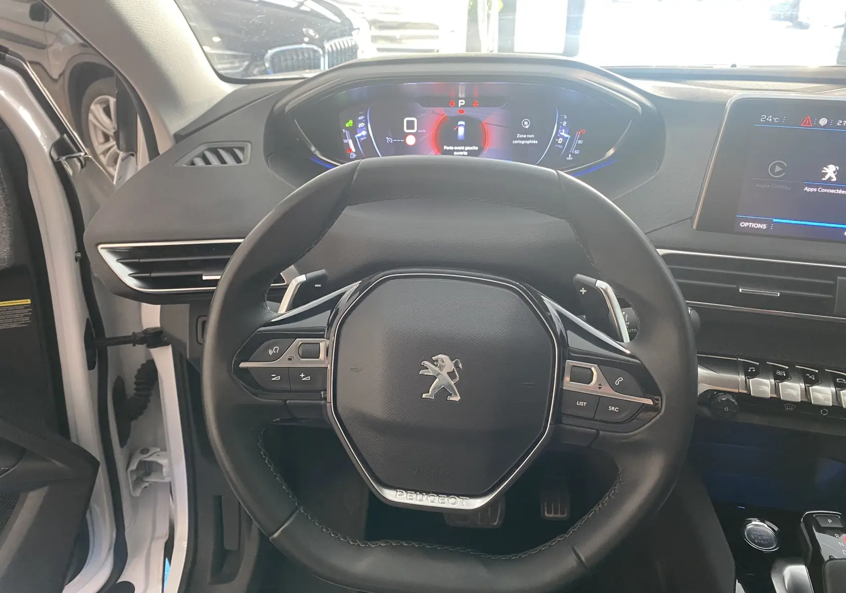 Vue intérieure centrée sur le volant cuir noir et le tableau de bord numérique du Peugeot 5008 blanc.