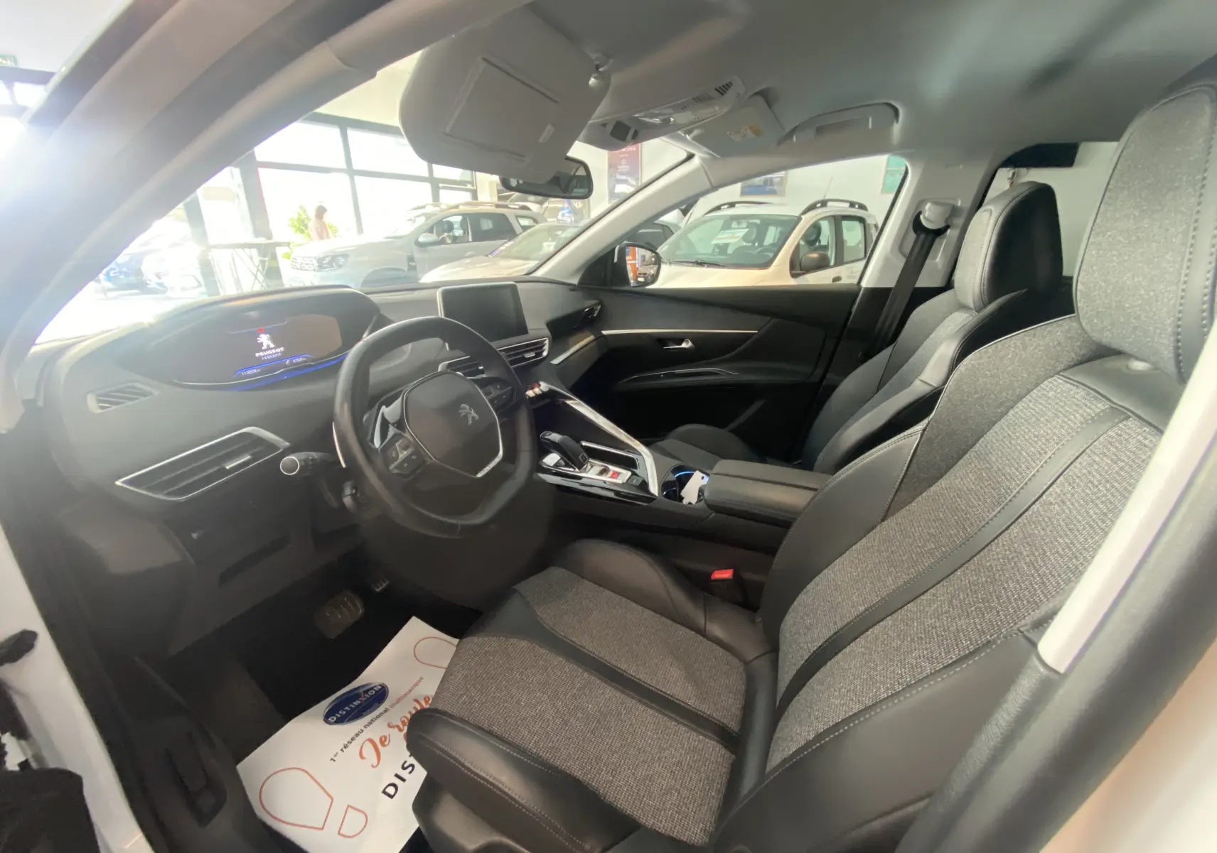 Intérieur avant droit du Peugeot 5008 blanc, sièges gris tissu et cuir, tableau de bord moderne avec écran tactile.