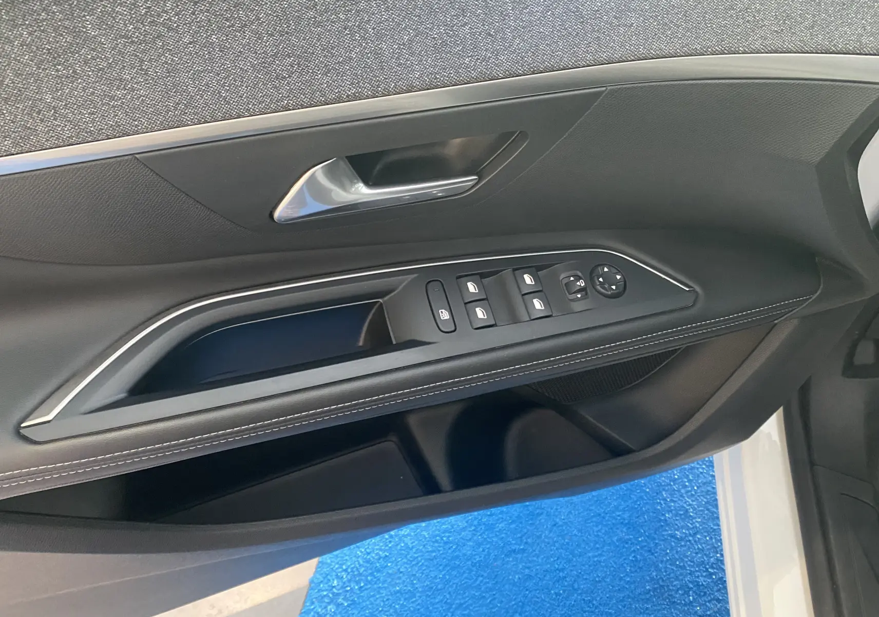 Vue rapprochée de la portière avant gauche noire du Peugeot 5008 blanc, avec commandes des vitres et poignée argentée.
