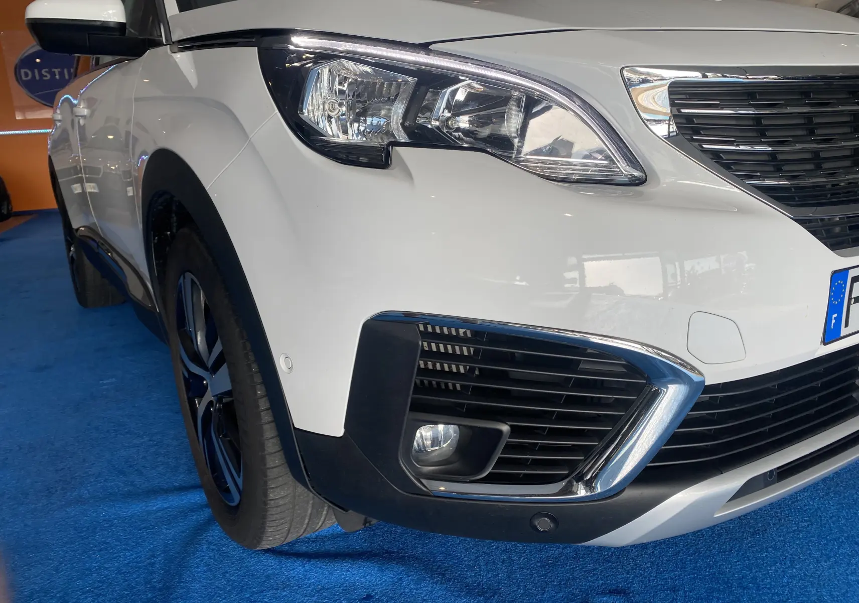 Gros plan sur l'avant droit blanc du Peugeot 5008 avec phares et calandre chromée visibles.