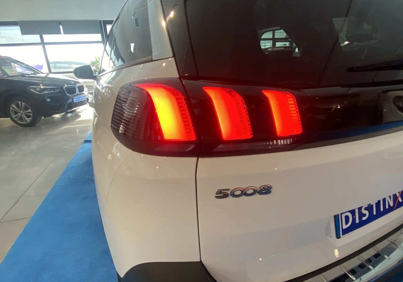 Feu arrière droit allumé sur Peugeot 5008 blanc Blanquise, vue arrière en intérieur de showroom.