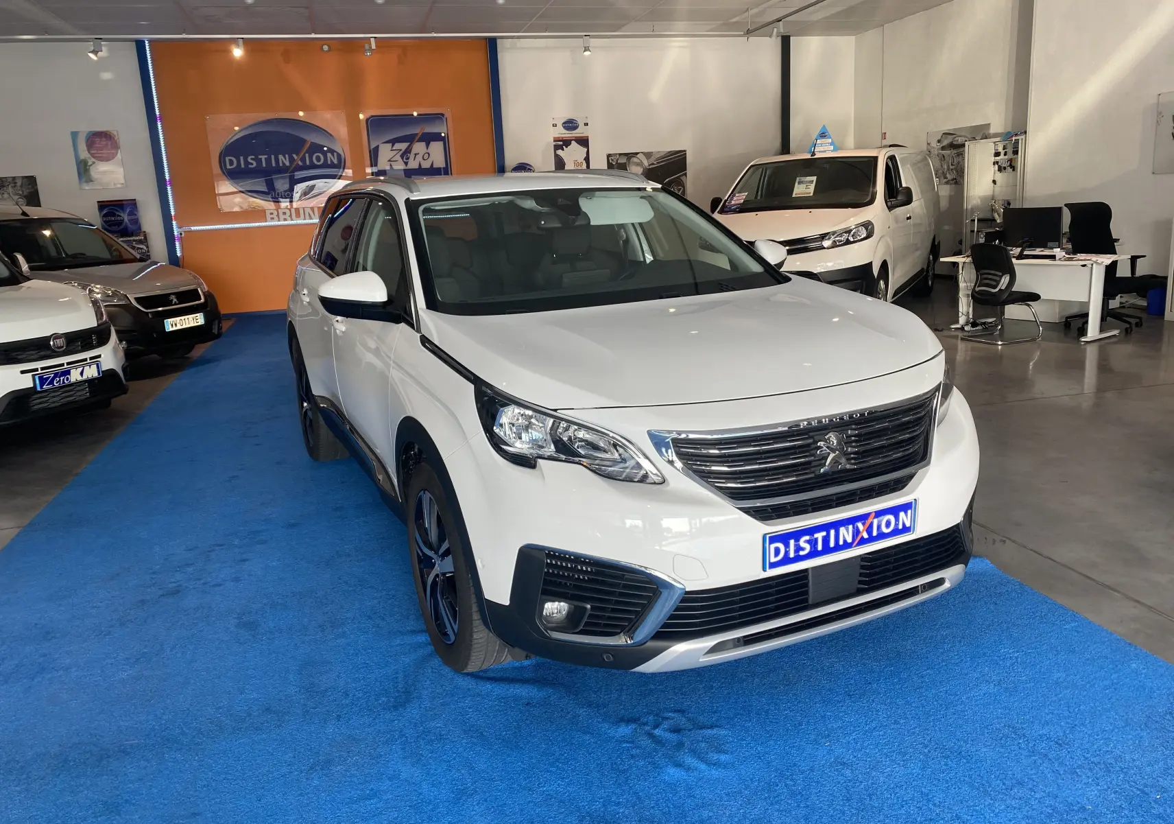 Peugeot 5008 blanc blanquise vue 3/4 avant droit avec attelage neuf dans un showroom intérieur.