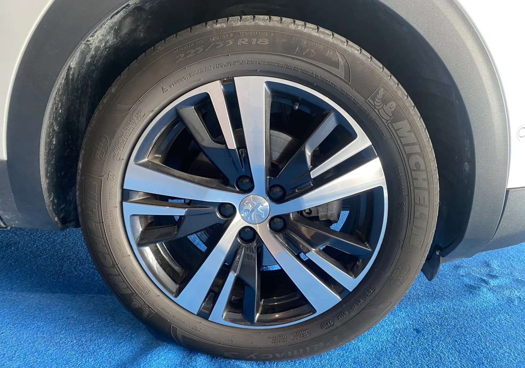 Gros plan sur la roue avant droite d'un Peugeot 5008 blanc Blanquise avec jante alliage bicolore et pneu Michelin neuf.