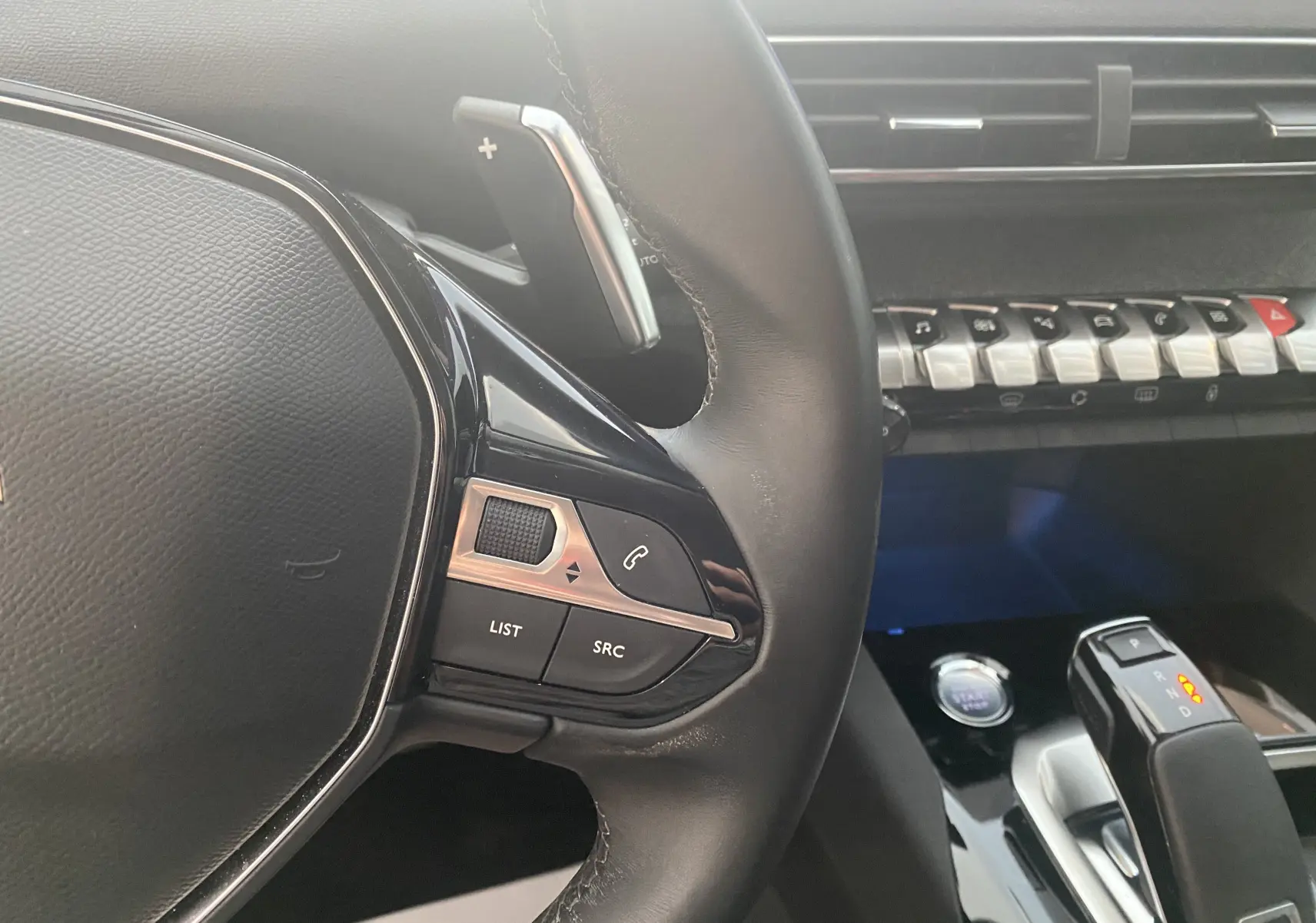 Gros plan sur le volant et la console centrale noire du Peugeot 5008 blanc, avec commandes au volant et levier de boîte auto visible.